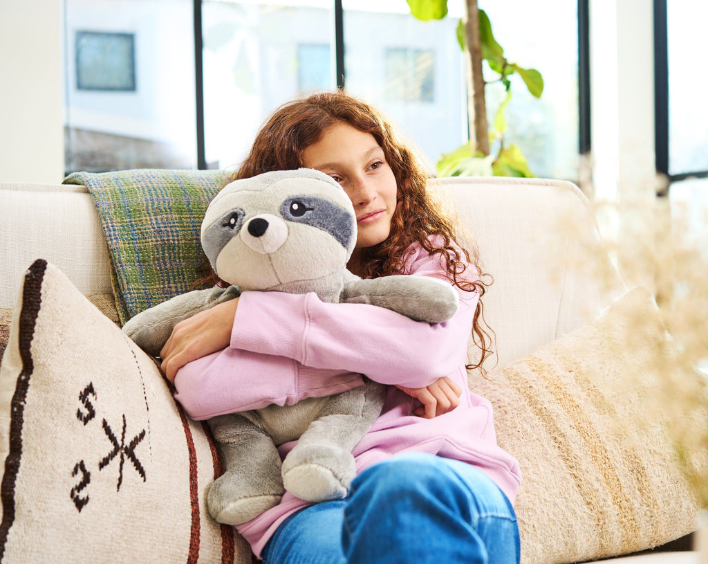 A little girl cuddles a sloth stuffed animal