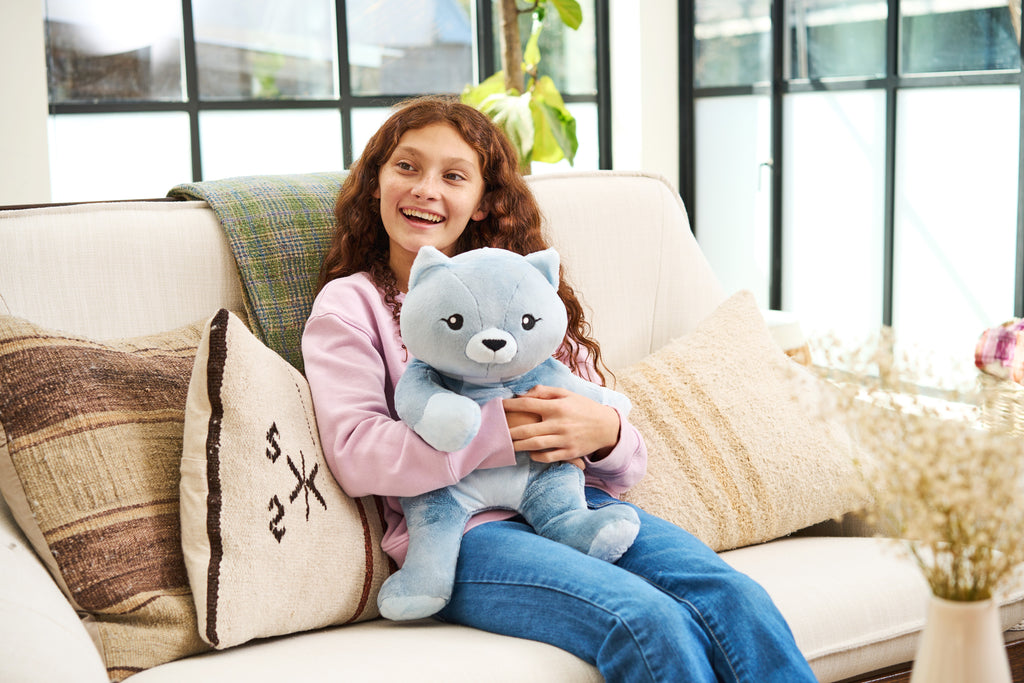 A little girl smiles as she holds a cat stuffed animal
