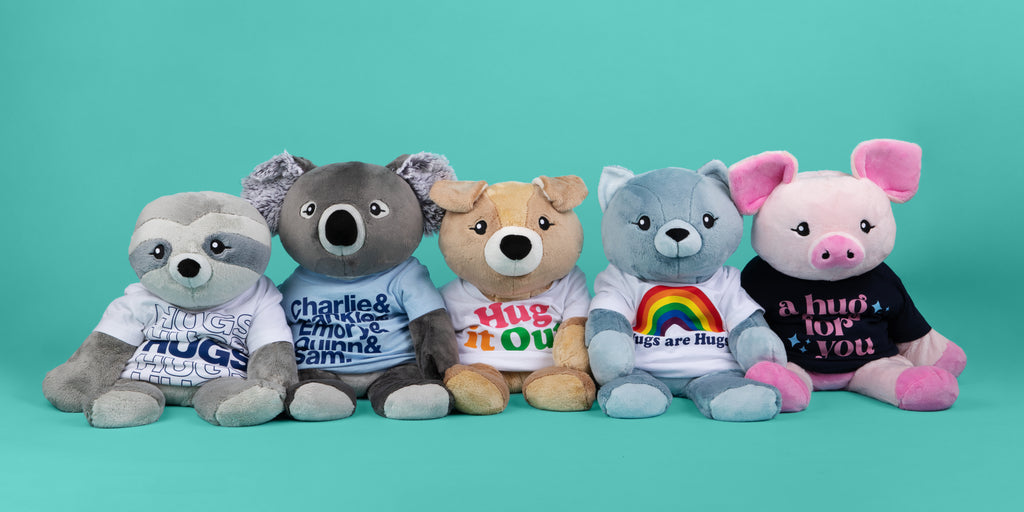 This image shows five Hugimals plushies wearing t-shirts, with a teal background.  From left:  Sam the Sloth, Quinn the Koala, Charlie the Puppy, Frankie the Cat and Harper the Pig.