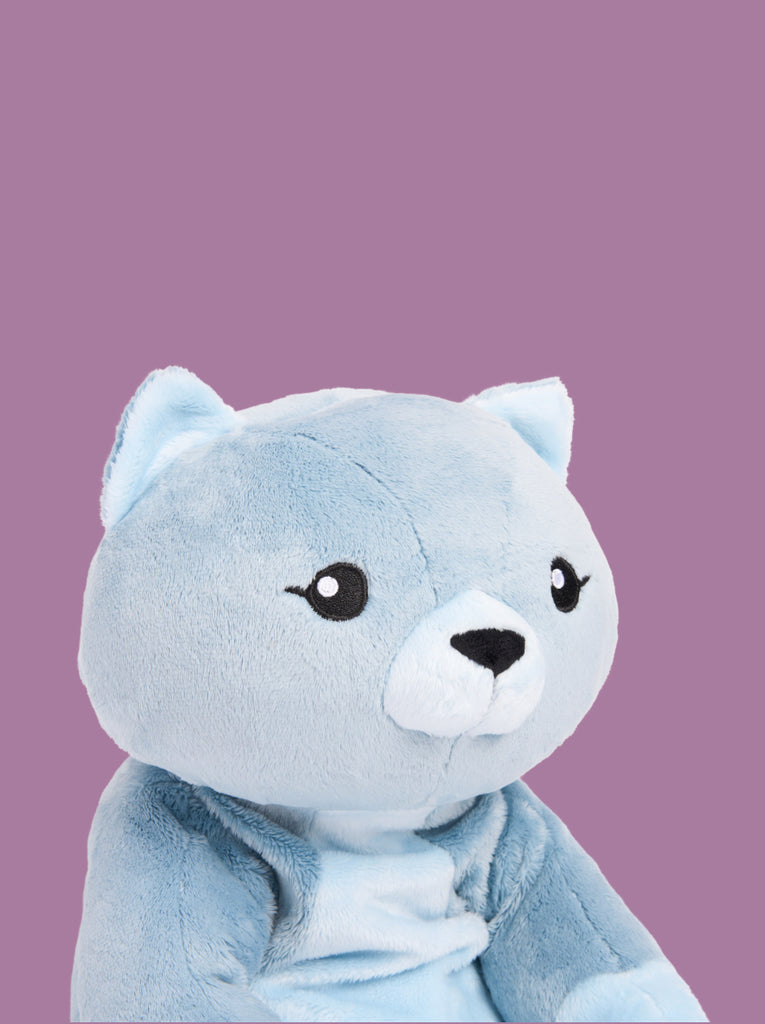 A closeup of the head and torso of a blue cat stuffed animal on a purple background