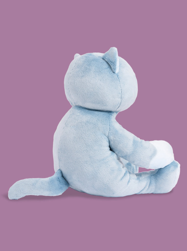 A blue cat stuffed animal sits facing away from the camera on a purple background