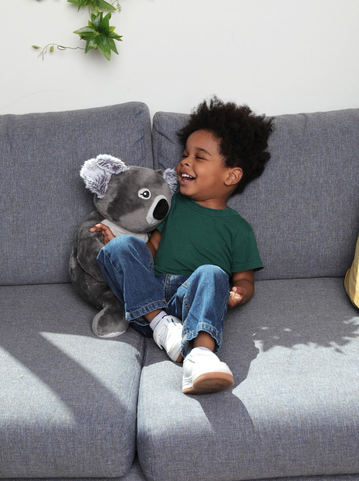 A litlle boy laughs while sitting close to a Koala stuffed animal