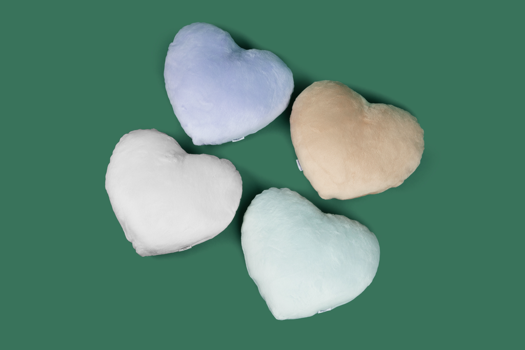Image shows four Heart to Hug Pillows arranged on dark green background: Lavender, Latte, Ivory, Mist