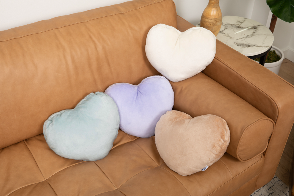 Image shows four Heart to Hug Pillows arranged on couch: Mist, Latte, Lavender, and Ivory