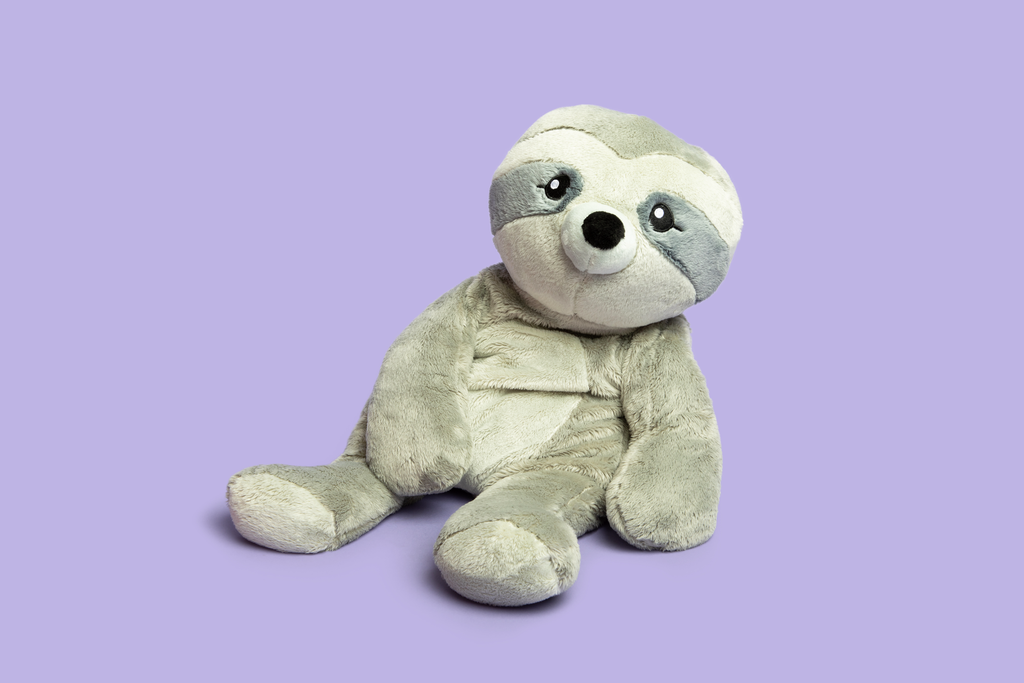 This photo shows Sam the Sloth Hugimal in a cute seated pose, looking at the viewer, on a purple background