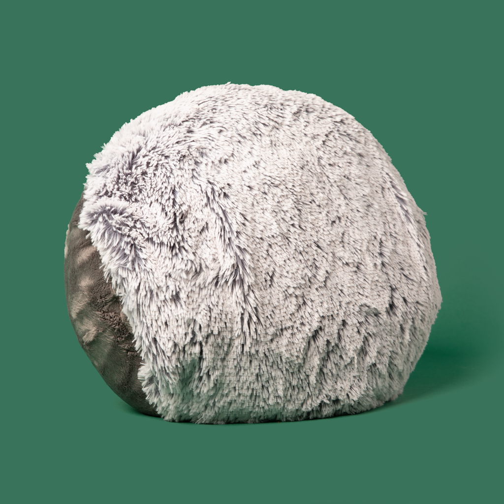 This photo shows our Hug Pillow on a green background. Visible is its light gray side (longer plush), and a bit of the dark gray side (shorter plush), as well as a peek a the hand pocket.