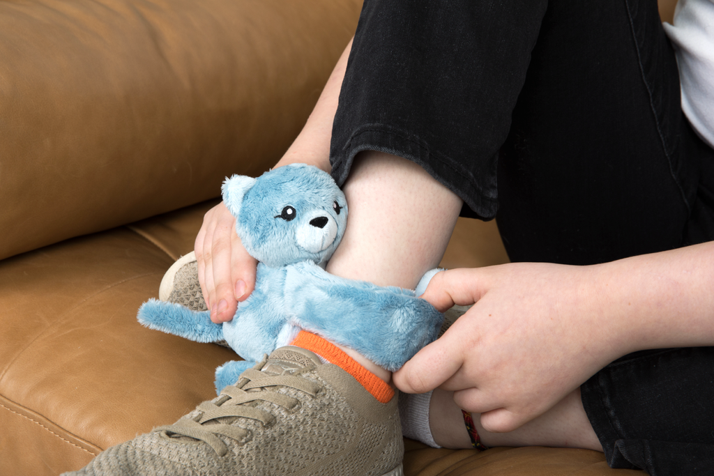 This photo shows a Cat Hug Baby with its arms wrapped around the ankle of a child, with the child holding the toy.