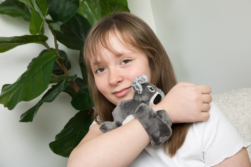 Seen here is a little girl smiling at the camera with a Koala Hug Baby around her wrist.