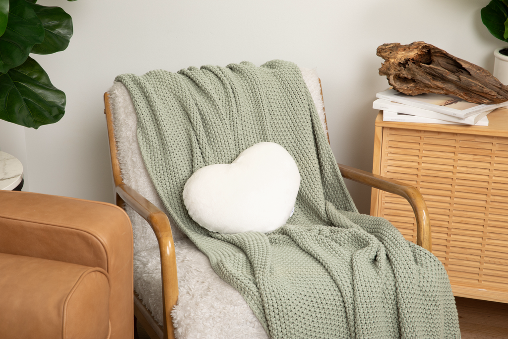 Image shows Ivory Heart to Hug PIllow on light green blanket on white chair