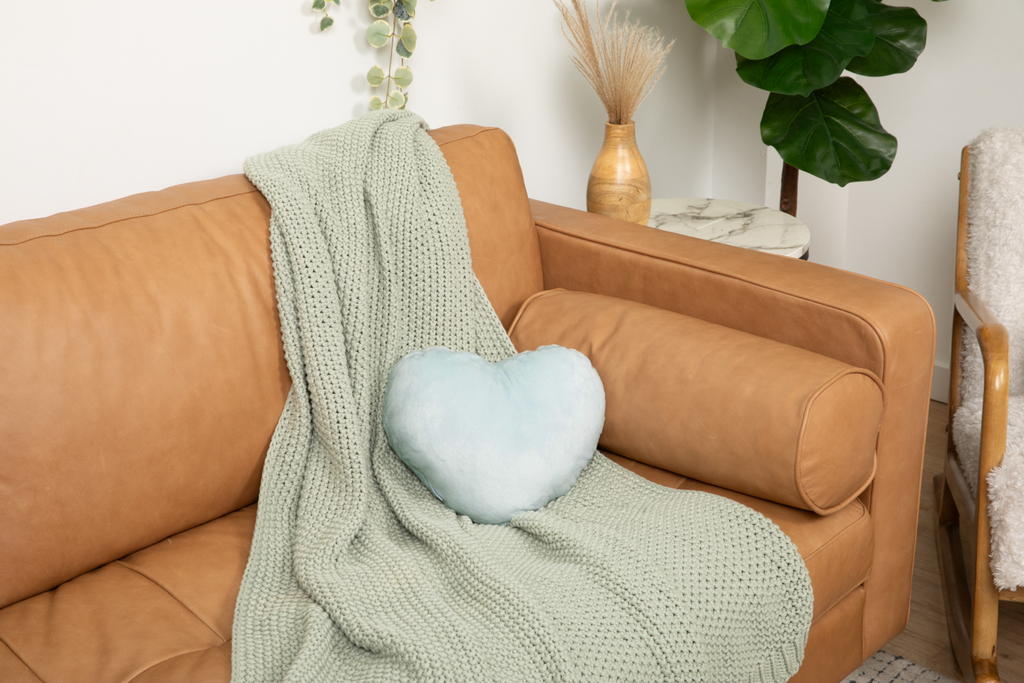 Image shows Mist Heart to Hug Pillow on a light green blanket on a tan couch