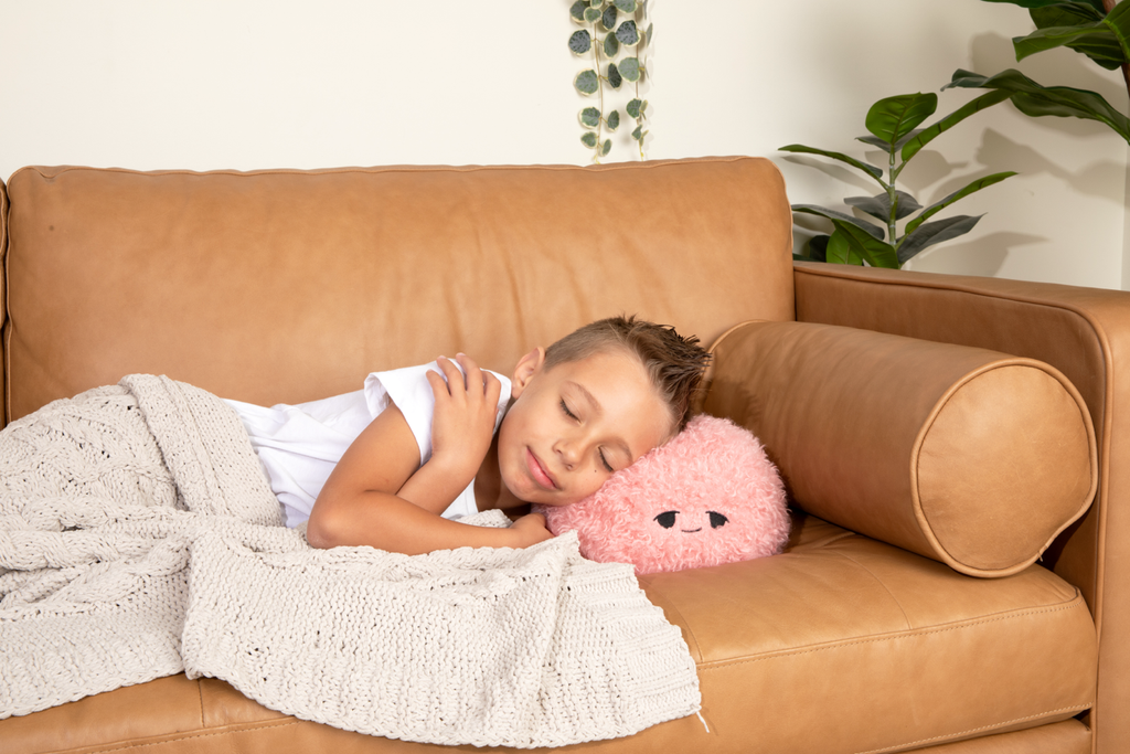 This photo shows a little boy sleeping on the couch, with his head resting on the Pink Hug Ball, showing it's "Sleepy" expression