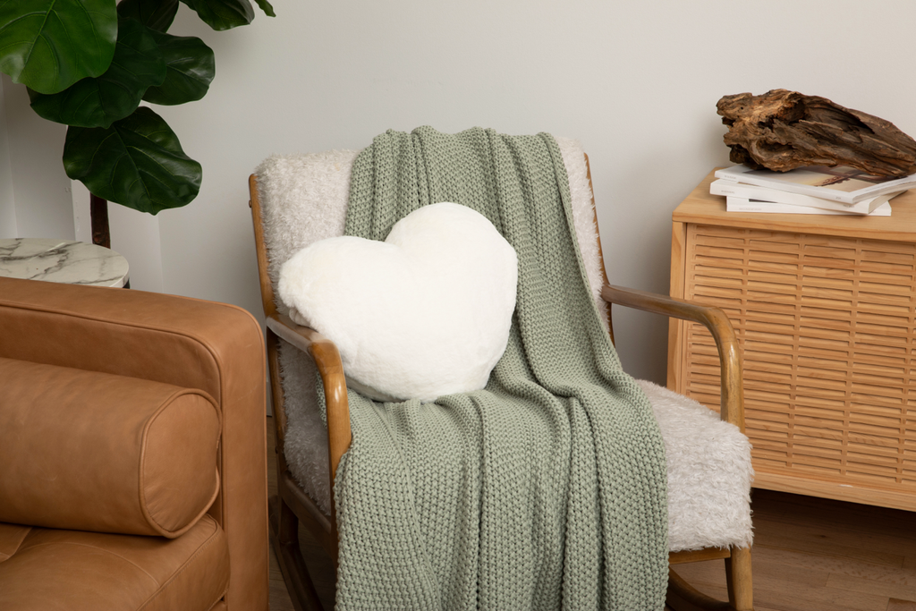 Ivory Super Sized Heart to Hug Pillow resting on white chair with green blanket